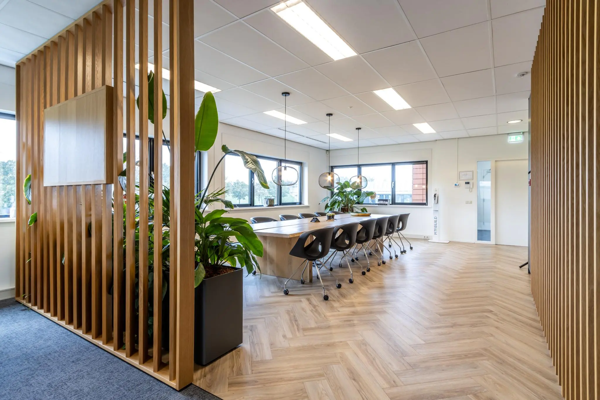 Modern ingerichte vergaderruimte aan de Lage Biezenweg met houten vloer, lange tafel, designstoelen en grote planten.